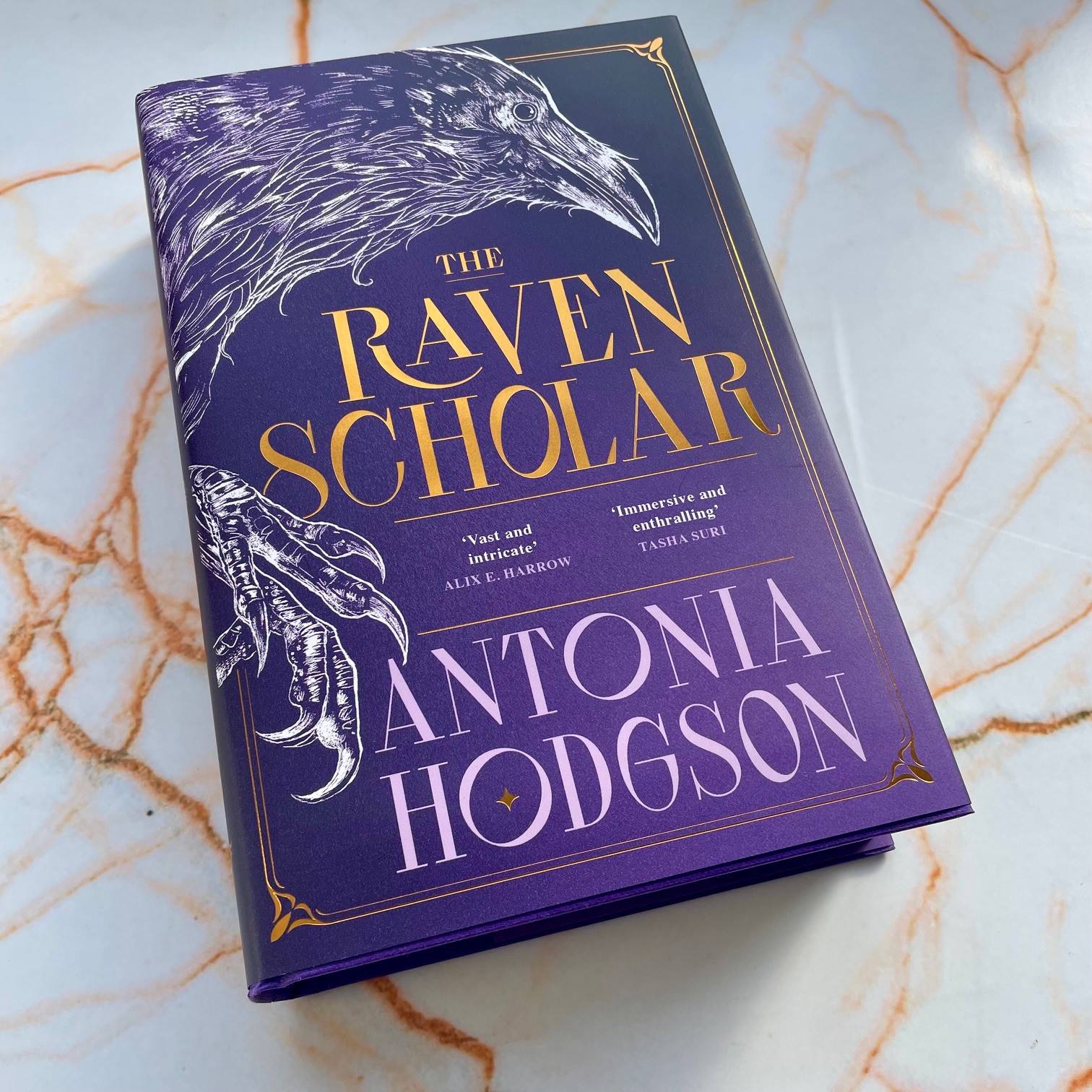 photo of Raven scholar book, purple with white line drawing of a raven. Title in gold foil. 